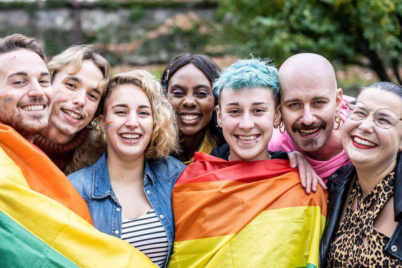Pride in Progress: How LGBTQ+ Professionals Are Redefining Success in 2025 A diverse group of young LGBTQ+ activists holding rainbow flags and signs at a Pride rally, smiling and showing solidarity for LGBTQ+ rights.